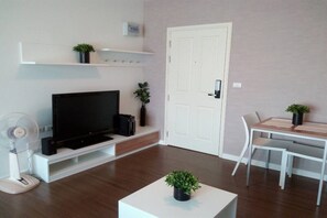 Una sala de estar con televisor de pantalla plana, una mesa de centro blanca con una planta, una mesa de comedor con sillas y una puerta blanca.