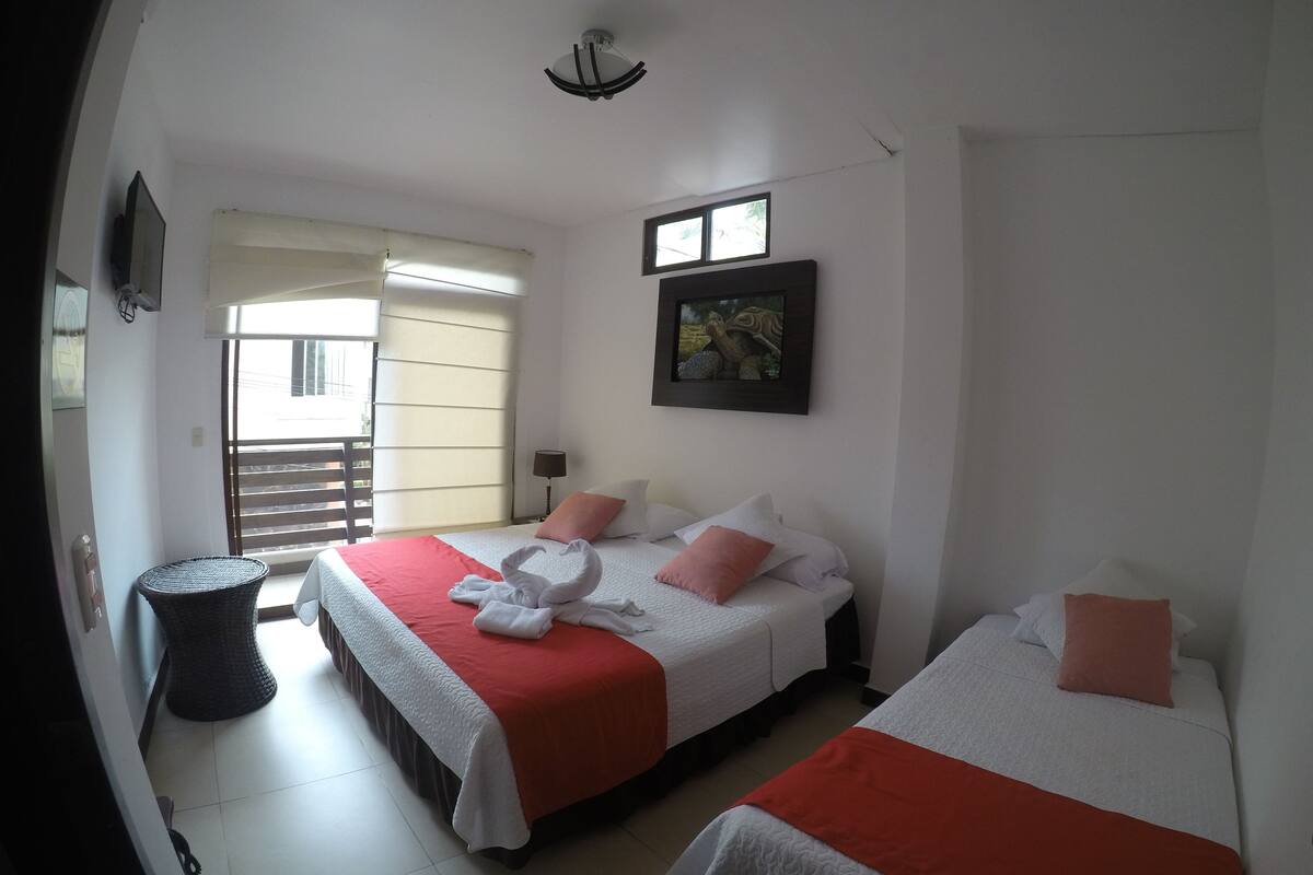 Een hotelkamer met twee bedden, een klein balkon, een schilderij aan de muur en een plafondventilator.