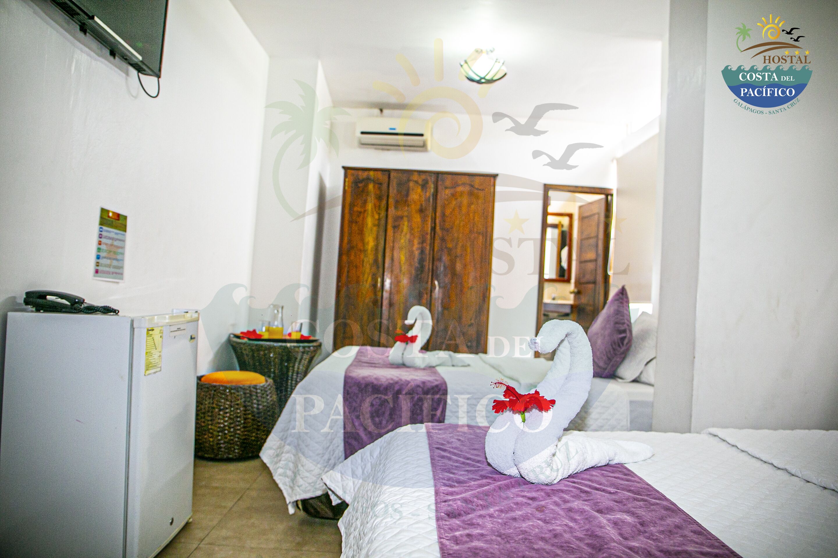 Quarto de hotel com duas camas, um frigorífico, uma cadeira de vime e um guarda-roupa de madeira.
