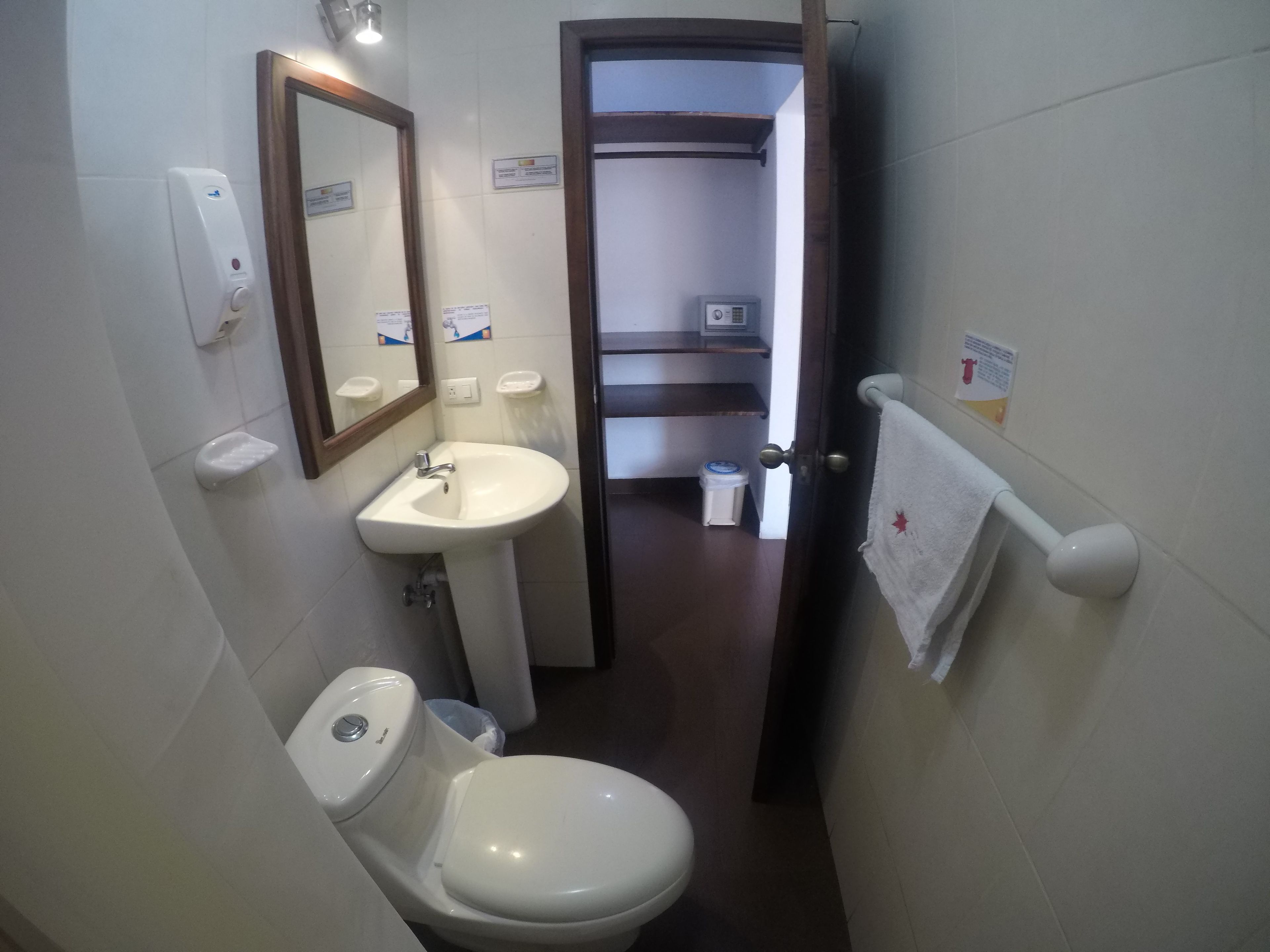 Une petite salle de bain avec un lavabo blanc, des toilettes et un miroir. On peut voir un porte-serviettes avec une serviette sur la droite.