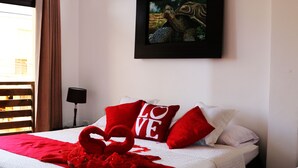 Une chambre d’hôtel avec deux lits, une literie rouge et blanche, un tableau encadré au mur et une fenêtre avec des rideaux.