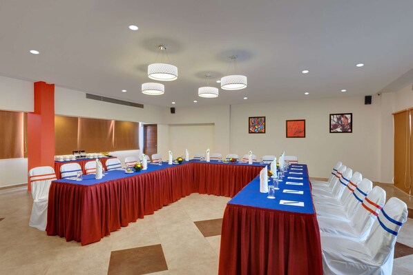 A conference room with a long table, white chairs with red and blue sashes, and modern pendant lighting. - Best Western Alkapuri, Vadodara (Vadodara)