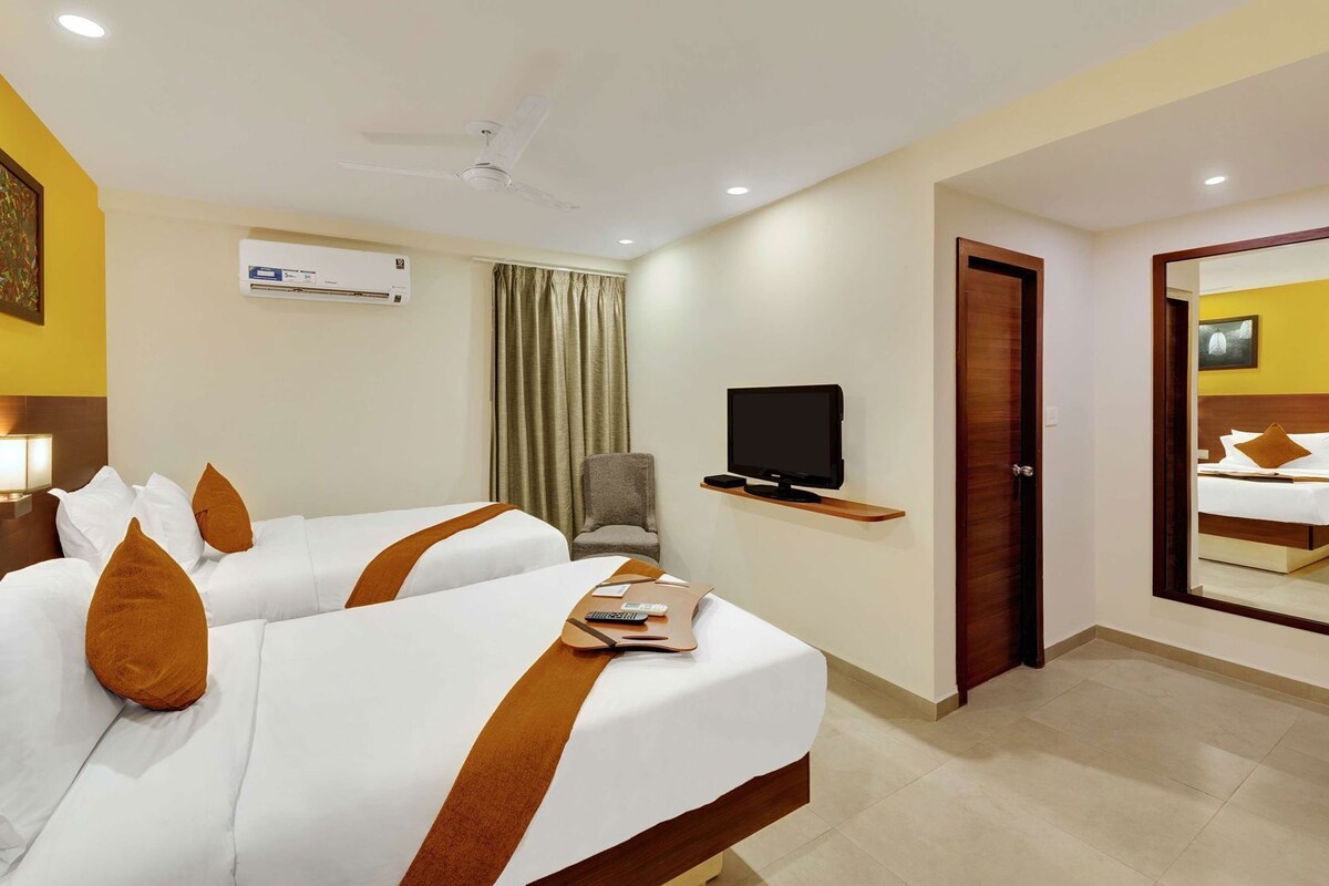 A hotel room with two beds, a TV, a chair, an air conditioning unit, and a door leading to another room.