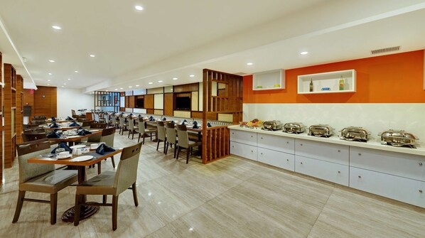 Un amplio comedor con varias mesas y sillas, una barra de buffet con recipientes de comida y un diseño de interiores moderno.