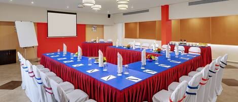 A conference room with a large rectangular table, white chairs with red and blue sashes, and a whiteboard on the wall.