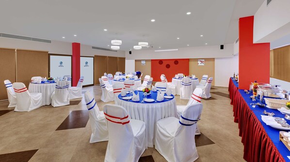A banquet hall with round tables, white chairs with red and blue sashes, and a red and white color scheme. - Best Western Alkapuri, Vadodara (Vadodara)