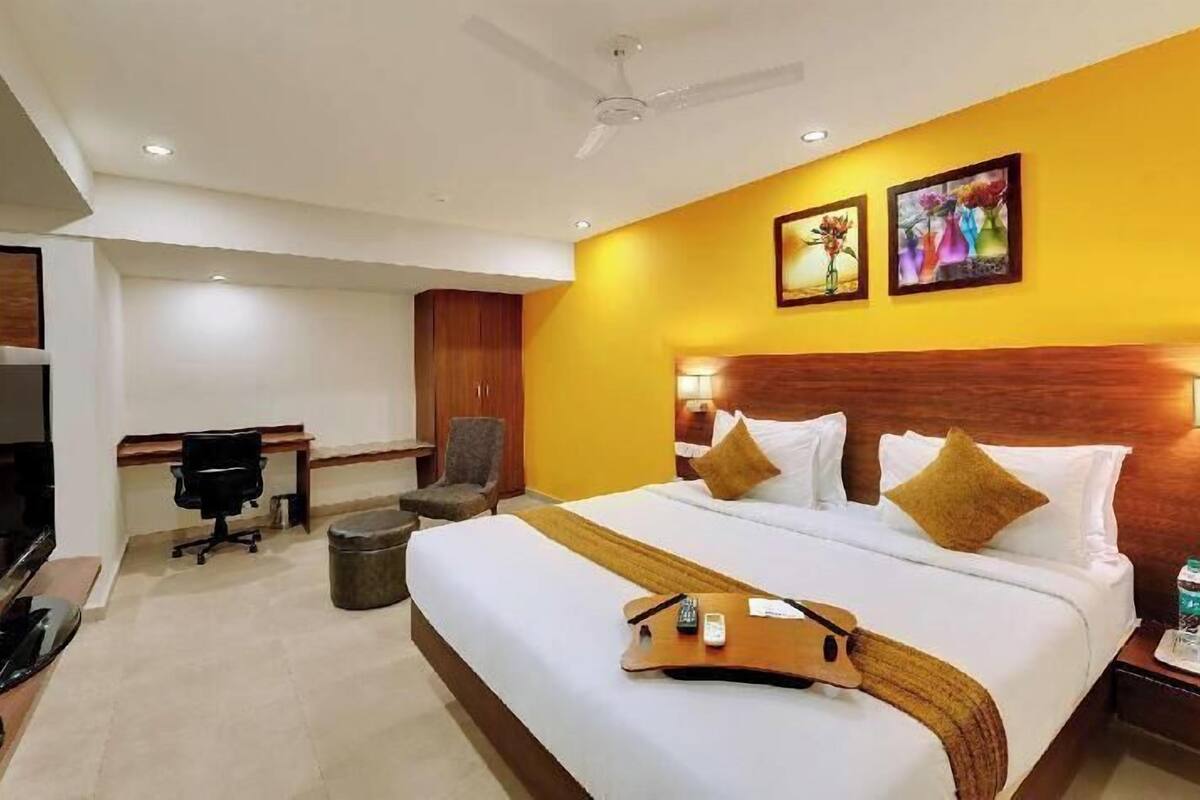 A hotel room with a bed, a desk, a chair, a television, and artwork on the wall.