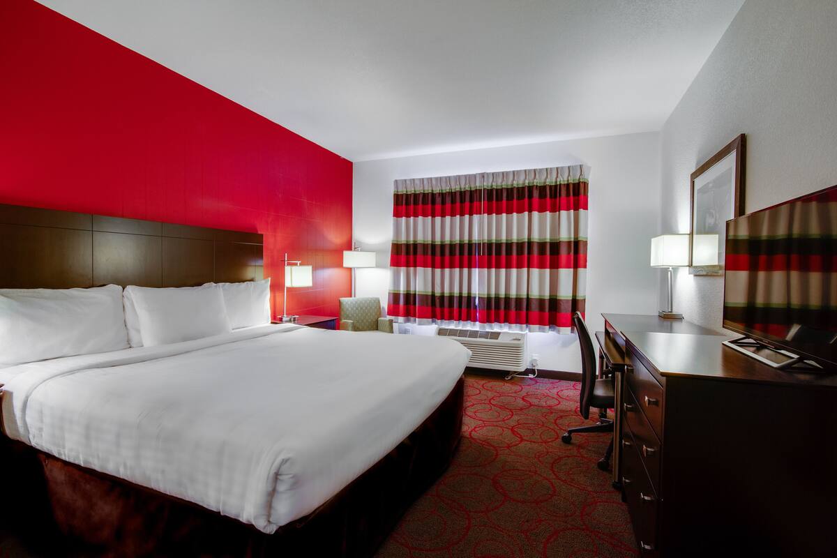 A hotel room with a large bed, a desk, a chair, a lamp, and a window with curtains.