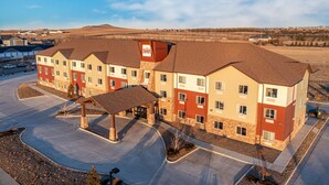 A multi-story hotel with a central courtyard, a covered entrance, and a visible parking area. - Inn at Hunters Run (Watford City)