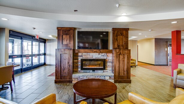 A lobby with a stone fireplace, leather seating, and a large TV screen. - Inn at Hunters Run (Watford City)