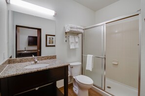 Une salle de bain avec un lavabo sur un comptoir en granit, des toilettes et une douche à parois de verre.