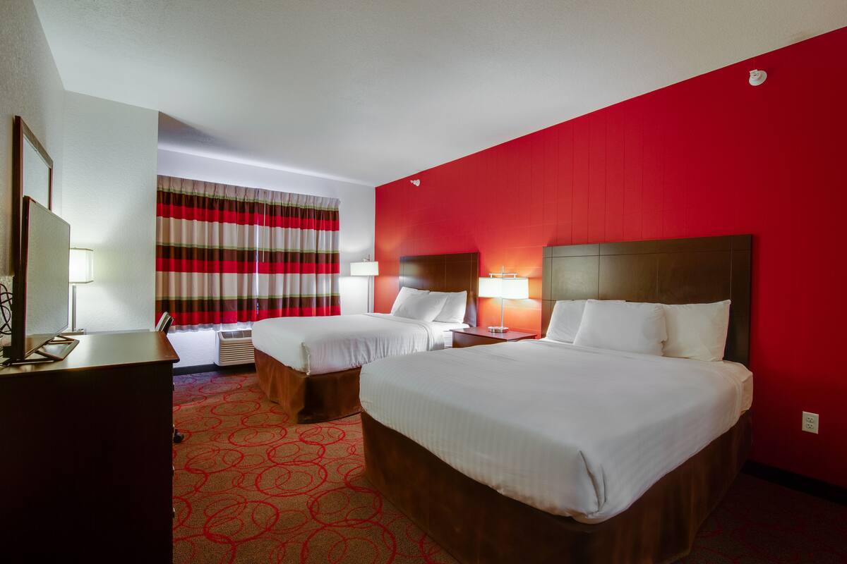 A hotel room with two beds, a desk, and a large window with striped curtains.