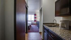A hotel room with a kitchenette, a bed, a desk, and a view of the city. - Inn at Hunters Run (Watford City)