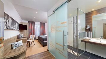 A modern hotel room with a bed, a sofa, a TV, and a glass partition with city names.