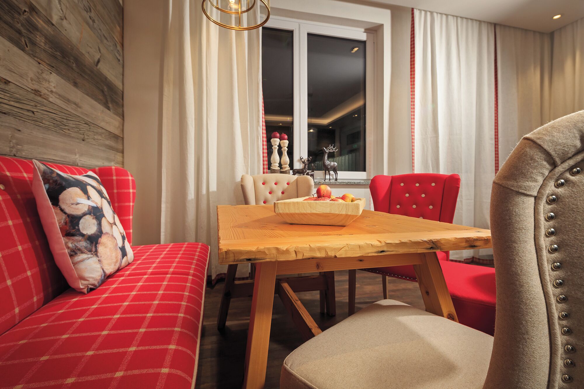 A cozy living room with a red sofa, a wooden dining table with a fruit bowl, and a red chair.