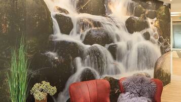 Un interno moderno con un'ampia murale a cascata, due poltrone rosse e un espositore in legno per piante.