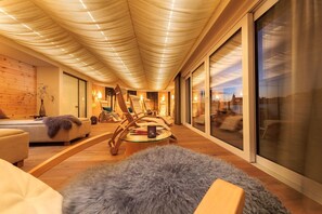 A modern living room with a curved ceiling, wooden flooring, and large windows offering a view of the cityscape. - Allgäu ART Hotel Kempten (Kempten)