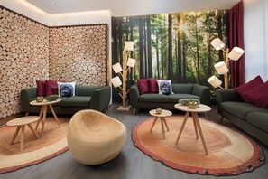 A modern living room with two green sofas, round wooden tables, and a unique wooden chair. - Allgäu ART Hotel Kempten (Kempten)