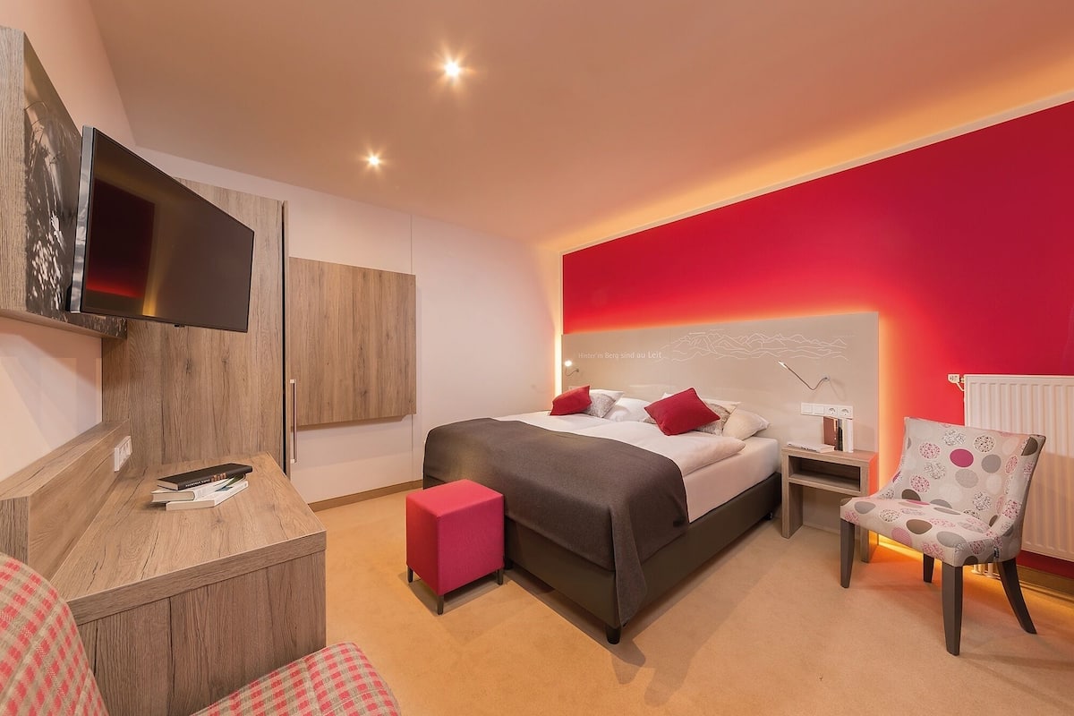 A modern hotel room with a bed, bedside tables, a TV, a desk, and a chair.