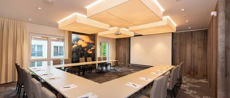 Un salón de conferencias con una larga mesa, sillas, una pantalla de proyector y un mural grande en la pared.