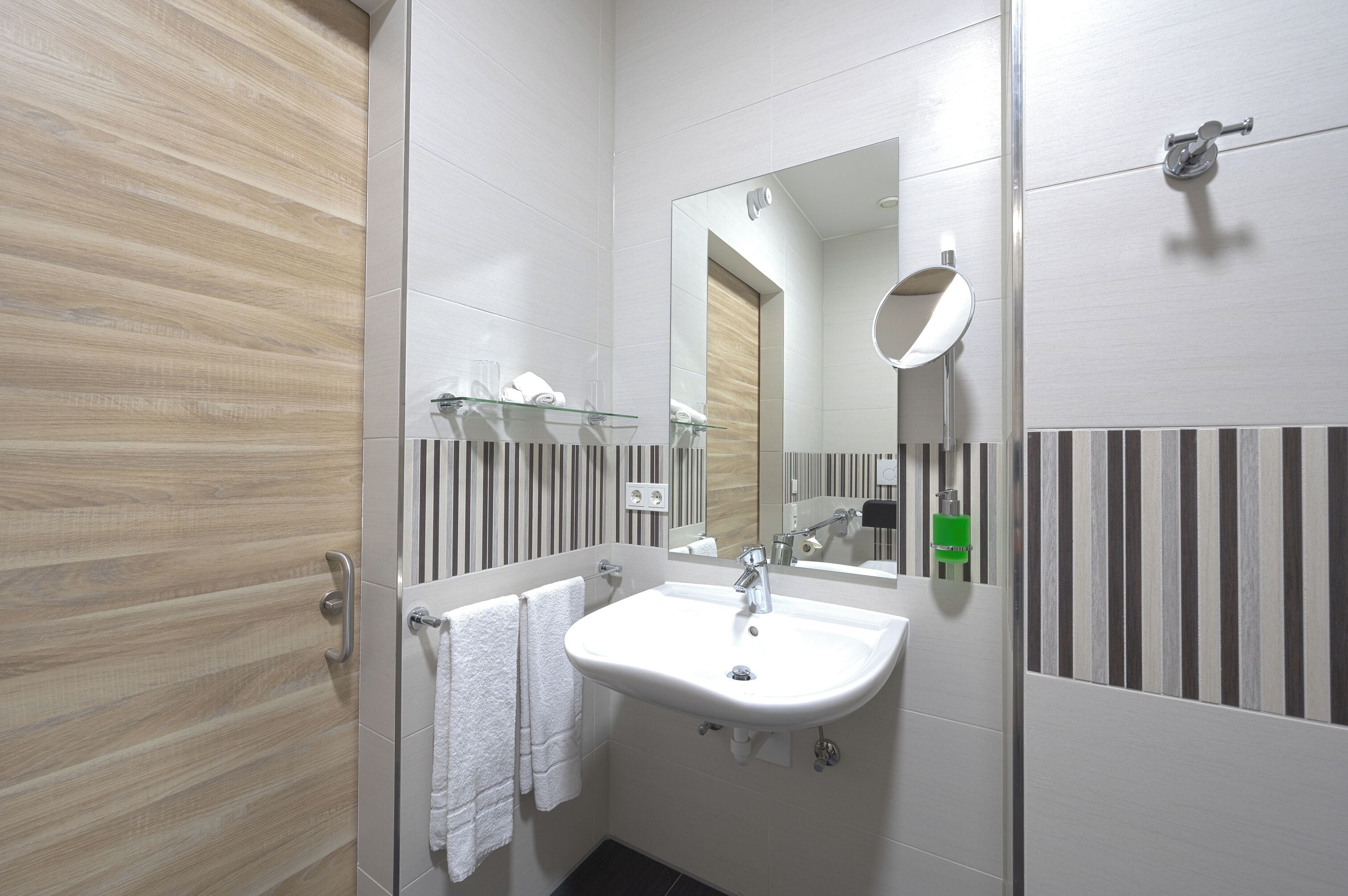 Un bany modern amb un lavabo blanc, una prestatgeria de vidre i un disseny de paret amb ratlles.
