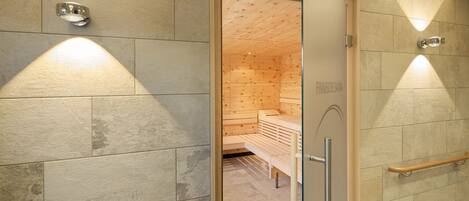 Un baño moderno con baldosas de piedra, bancos de madera y una puerta de cristal que da a un cuarto de sauna.