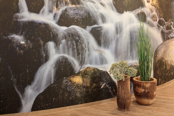 A wooden table with two potted plants and a wall mural of a waterfall. - Allgäu ART Hotel Kempten (Kempten)
