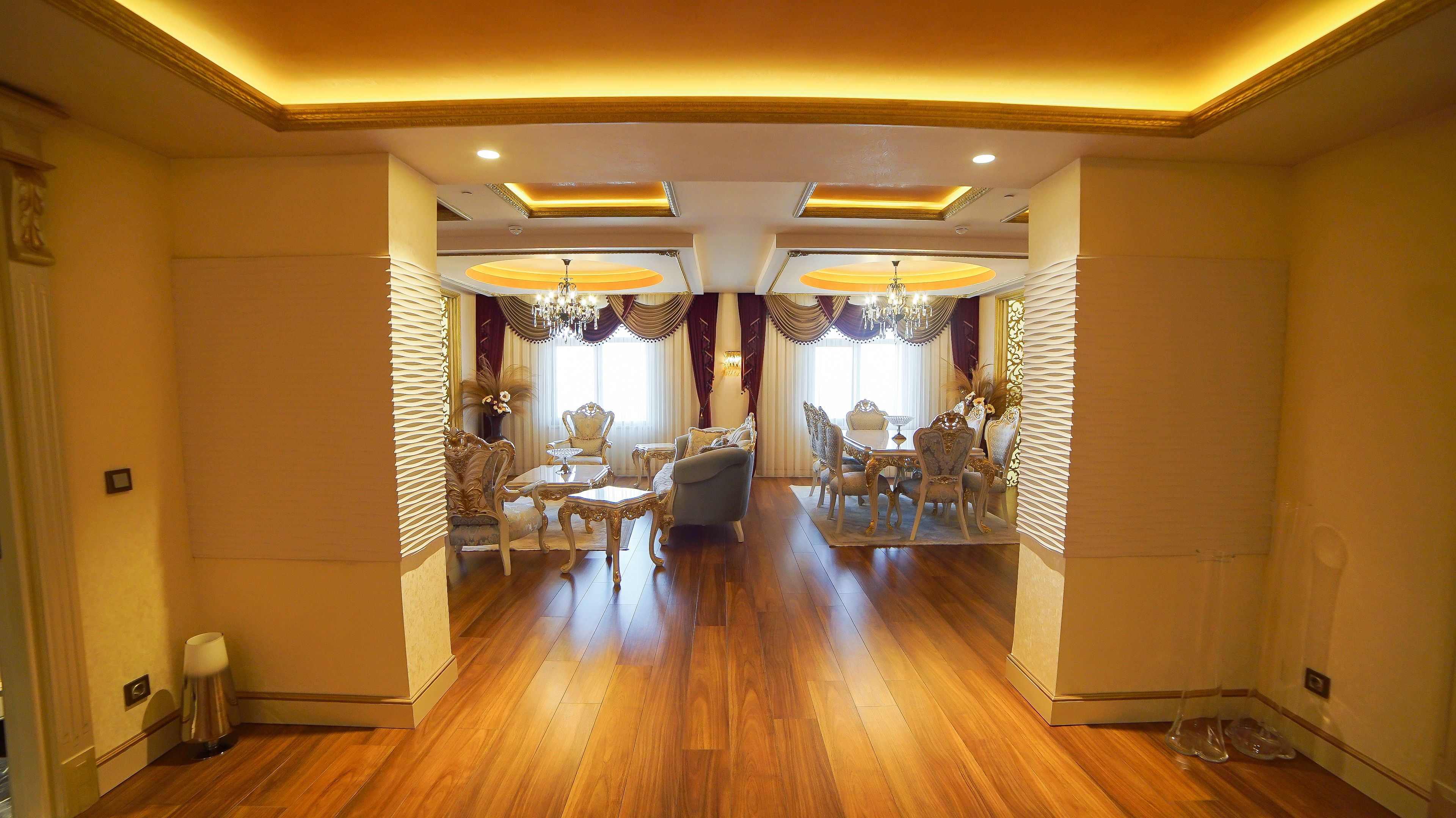 A spacious dining area with a long table and ornate chairs, a chandelier, and a decorative mirror on the wall.