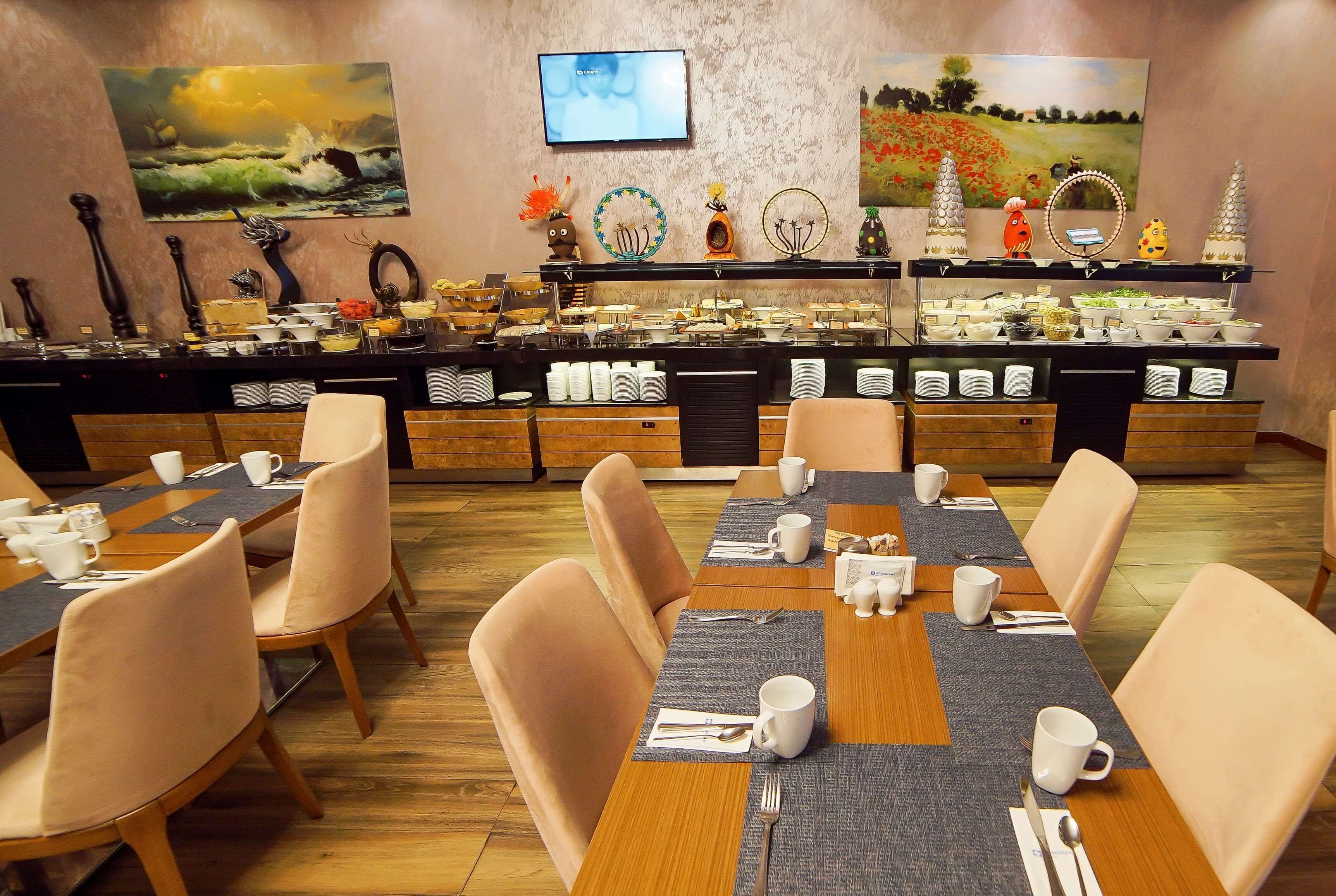 A dining area with multiple tables and chairs, a buffet with various food items, and artwork on the walls.