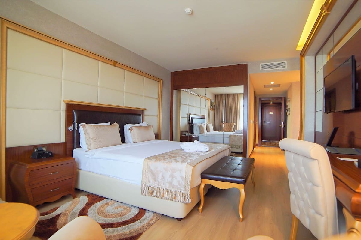 A hotel room with a large bed, a desk, a chair, a TV, and a bathroom visible through a mirror.