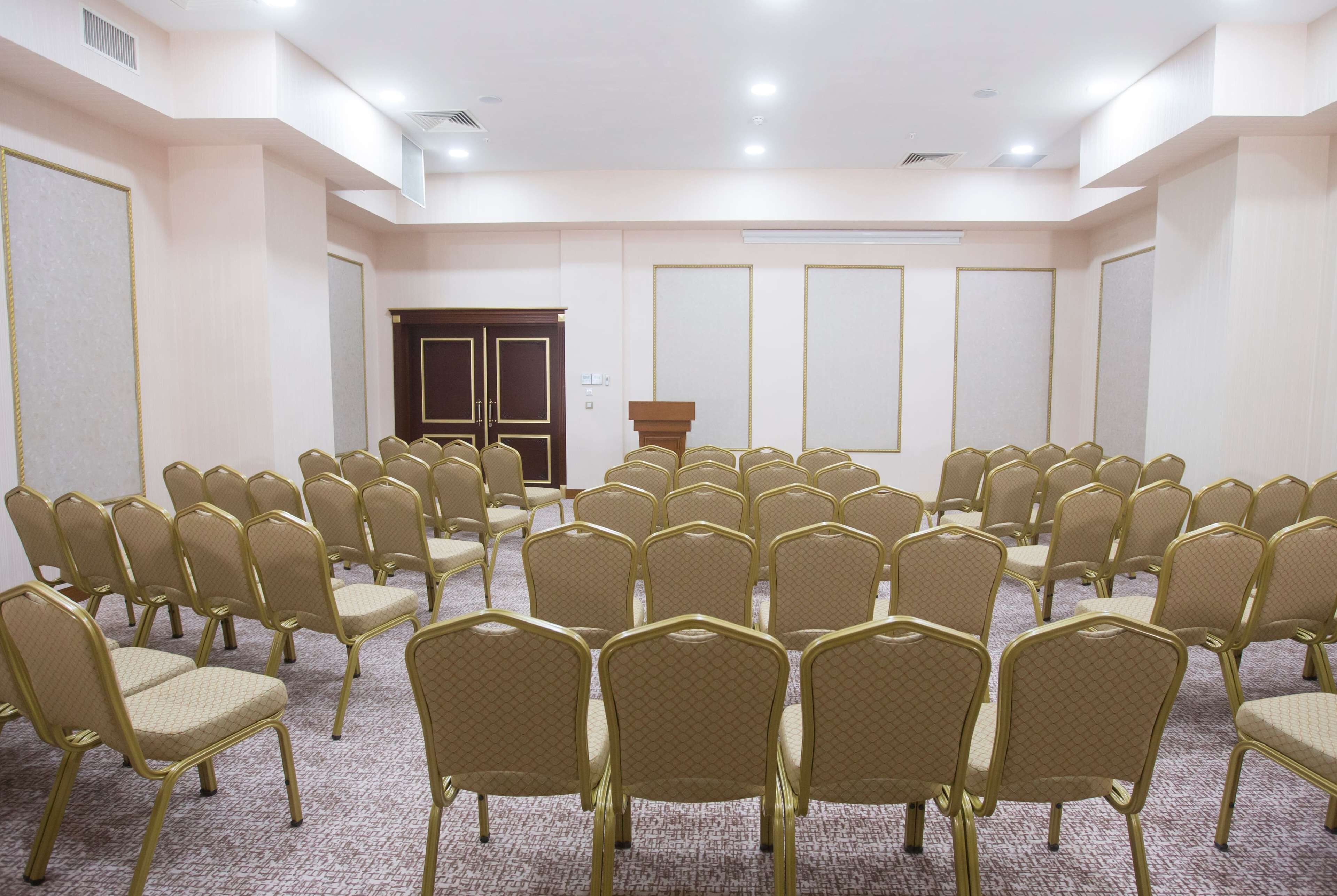 Un salón de conferencias con hileras de sillas, un atril y una puerta al fondo.