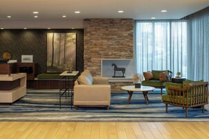 A modern hotel lobby with a stone accent wall, a reception desk, a seating area with a sofa and armchairs, and a large window with curtains.