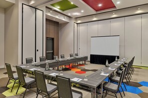 Ein Konferenzraum mit langem Tisch, Stühlen, einer Projektionsleinwand und einer Tür.