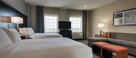 A hotel room with two beds, a television, a sofa, and a small table.