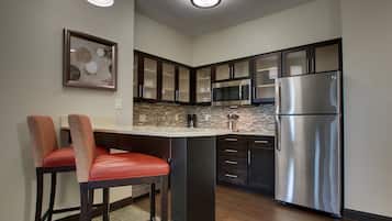 A modern kitchen with dark cabinets, a stainless steel refrigerator, and a bar area with two red chairs.
