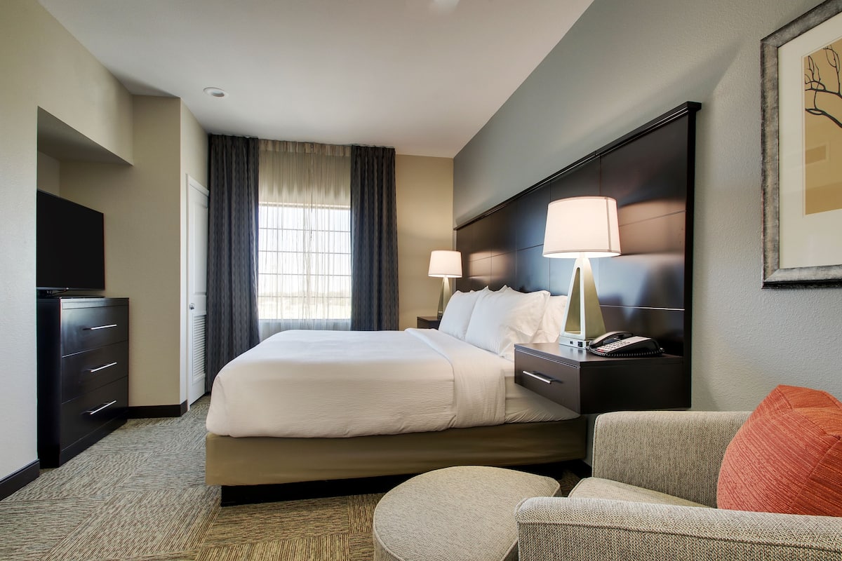 A hotel room with a large bed, two bedside lamps, a flat-screen TV, a desk with a lamp, and a chair.
