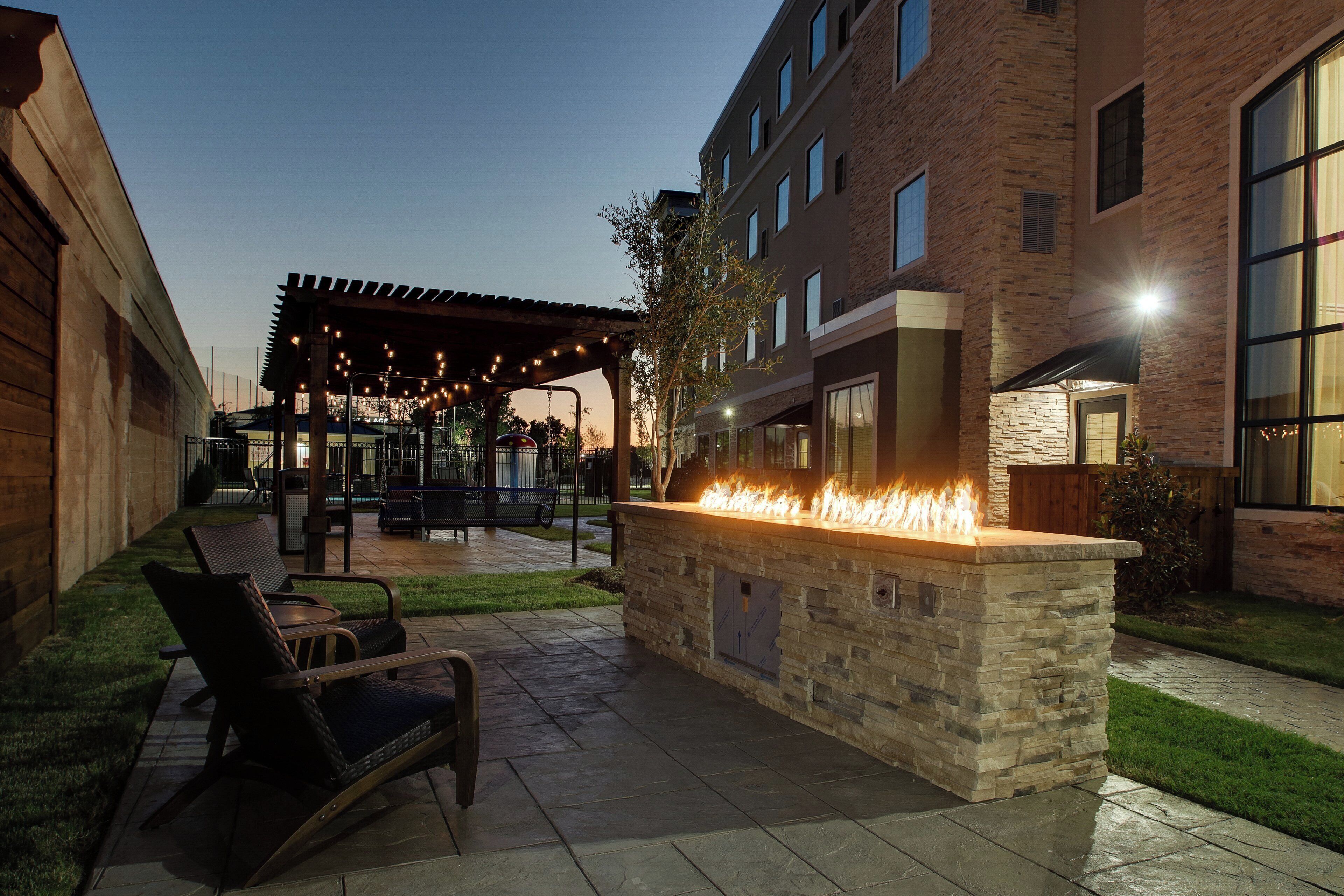 An outdoor patio with a stone fire feature, seating, and a covered area with string lights.