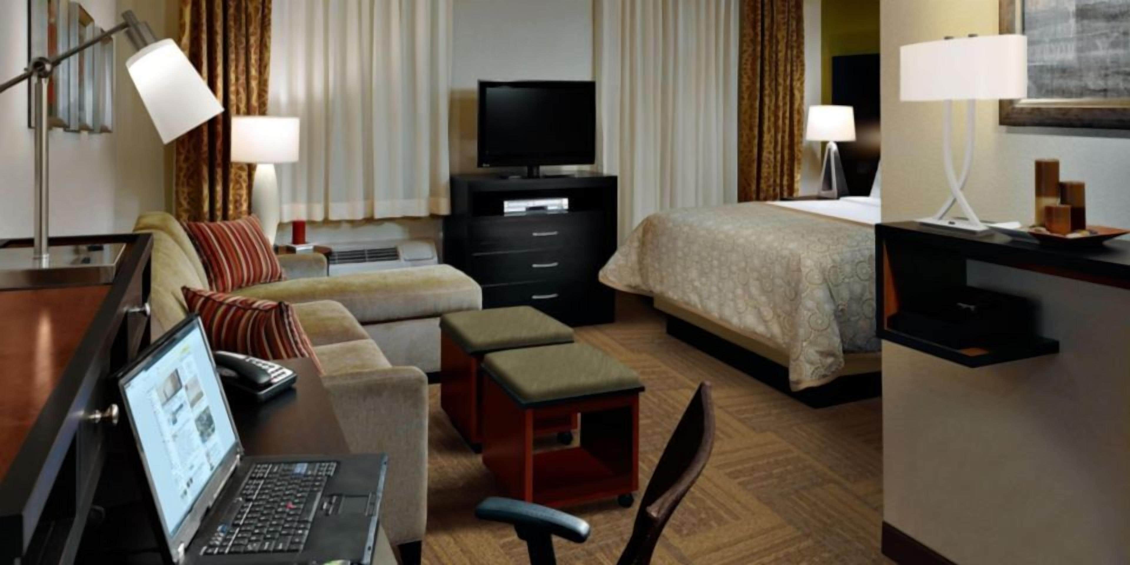 A hotel room with a bed, a sofa, a desk with a laptop, a TV, and a bedside table.