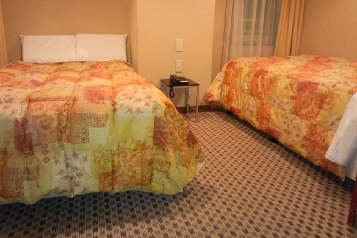 A hotel room with two beds, a small table, and a telephone.