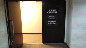 A closed door with a sign in Japanese, a metal handle, and a light source from the adjacent room.