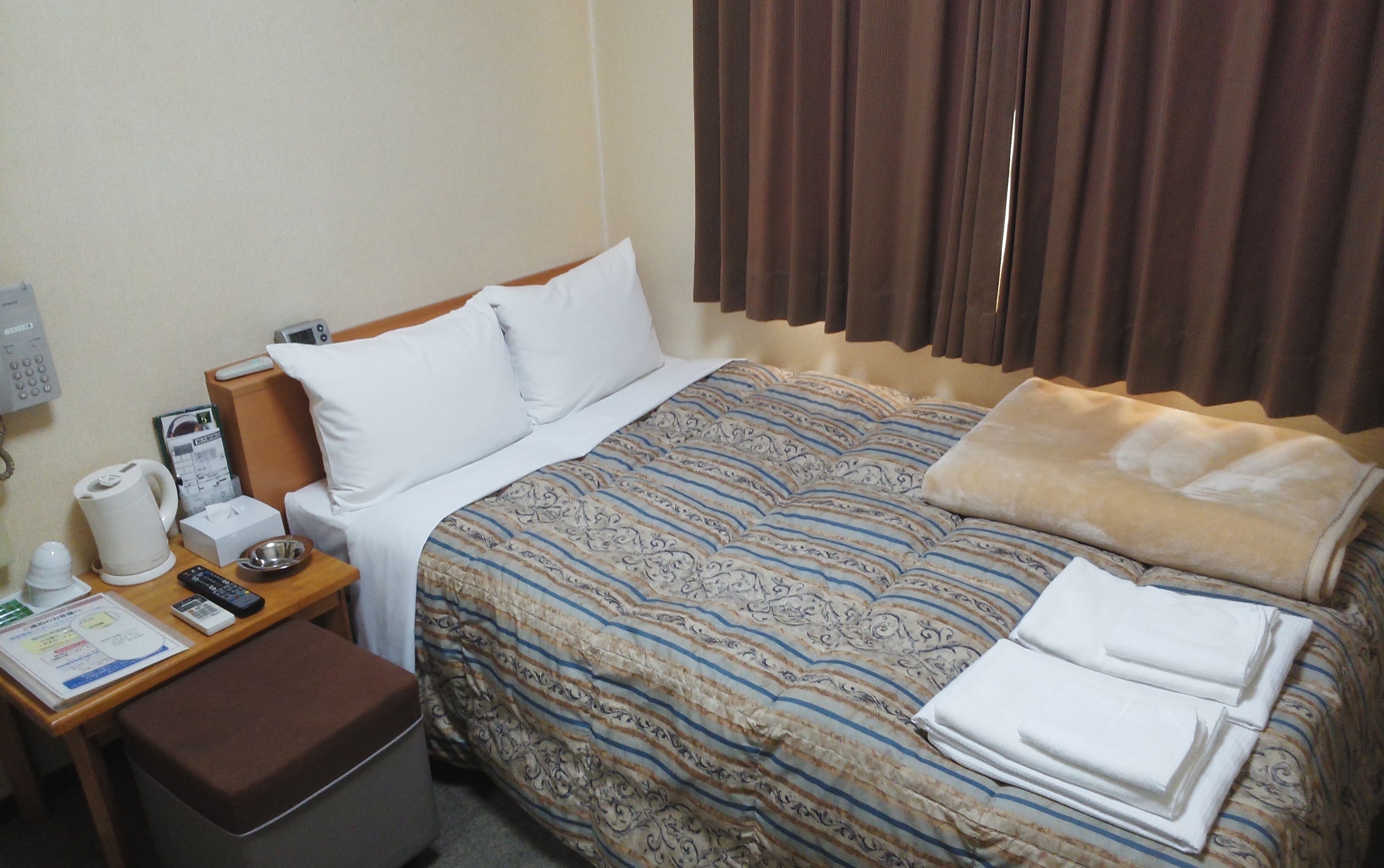 A hotel room with a bed, a desk with a telephone, a coffee maker, and a small table with a remote control.