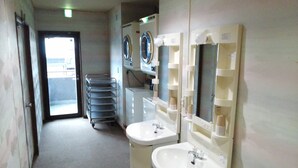 A narrow hallway with two sinks, a rack of towels, and a door leading to a brighter area.