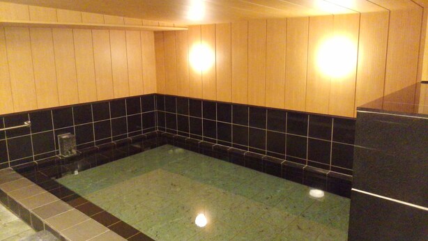 A bathroom with a bathtub, black and beige tiled walls, and a wooden ceiling.