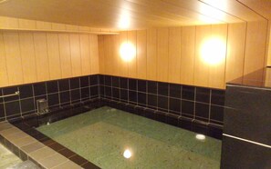 A bathroom with a bathtub, black and beige tiled walls, and a wooden ceiling. - Hotel Miyako Hills Stationten (Miyako)