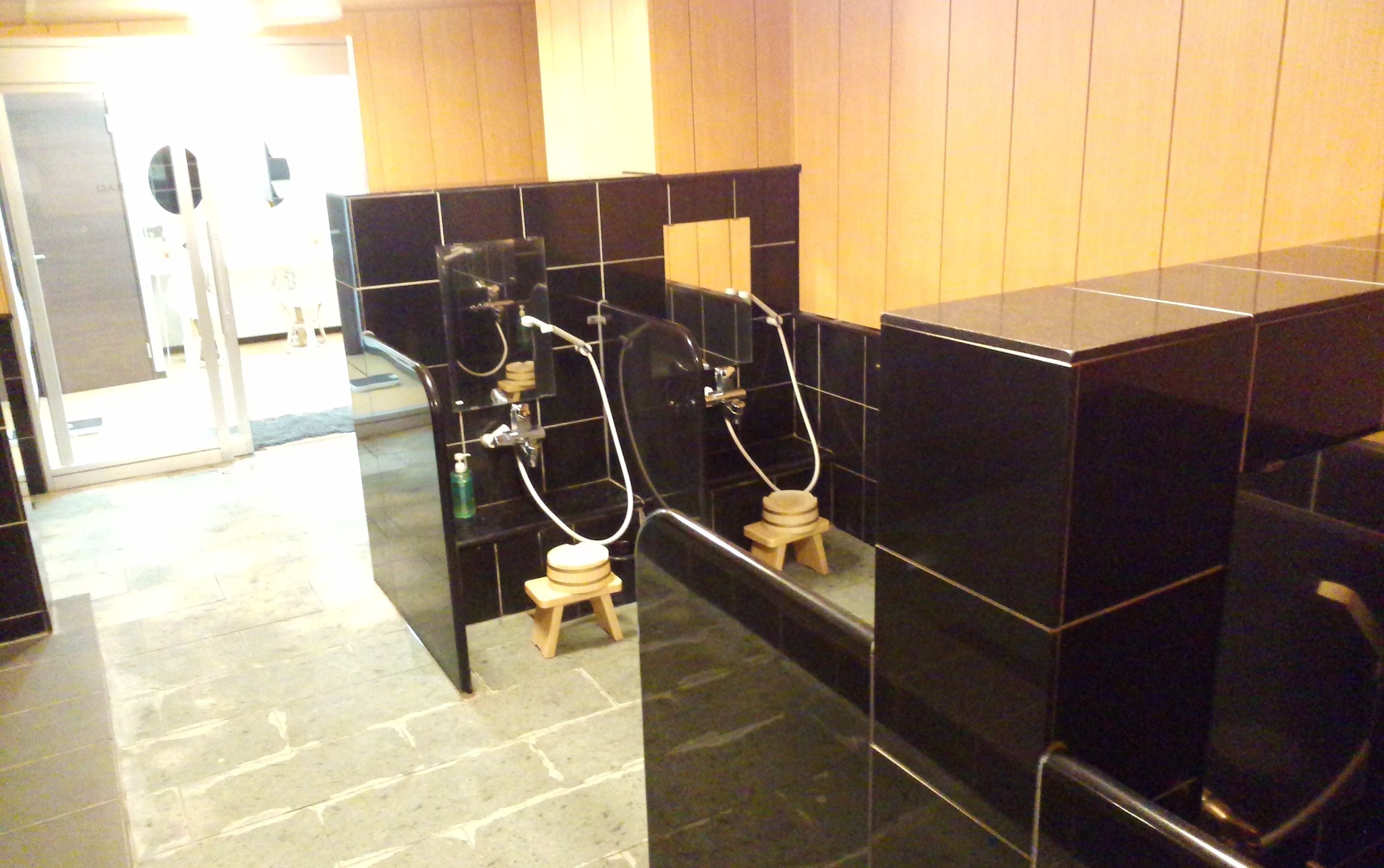 A public restroom with black tiled walls, a wooden floor, and a glass partition.
