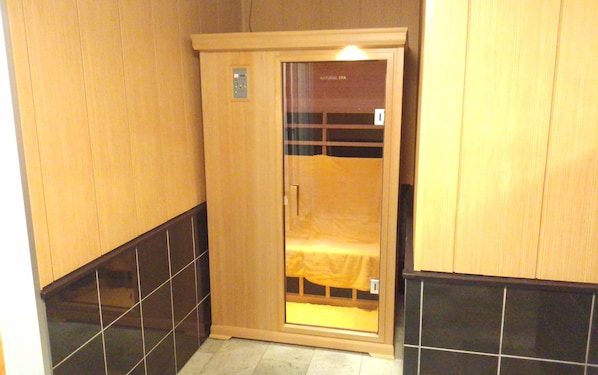 A wooden spa room with a glass door, tiled floors, and a bench inside.