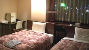 Een hotelkamer met twee bedden, een bureau, een stoel en een raam met gordijnen.