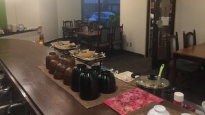 A dining area with a long table set for multiple people, a fire extinguisher, and a window with blinds. - Hotel Niihama Hills Prince House (Niihama)