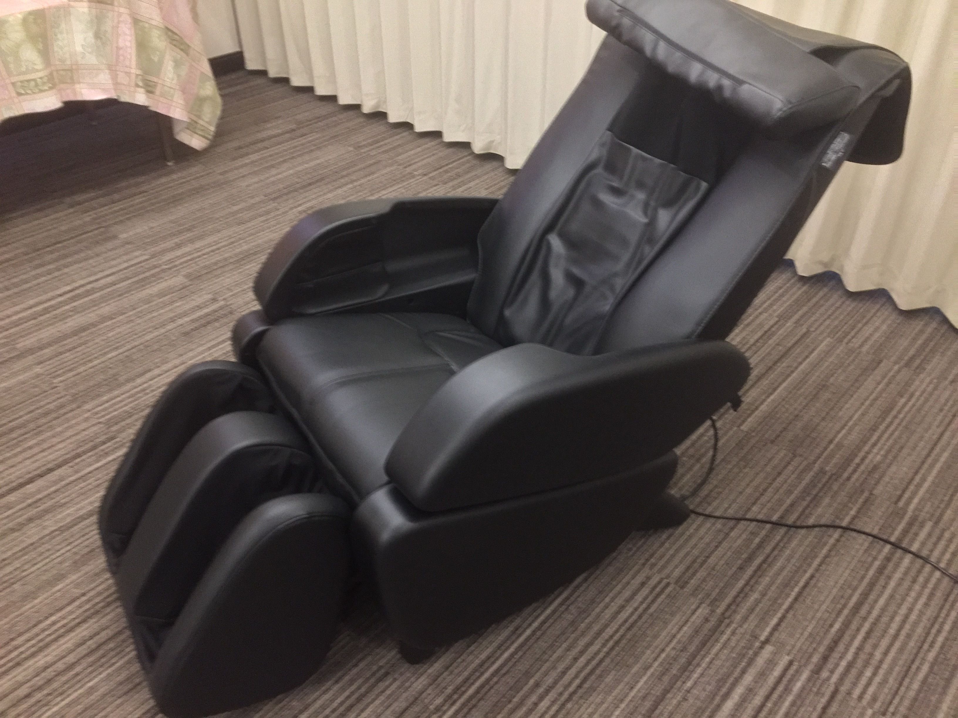 Een massagestoel in een kamer met vloerbedekking en een gordijn.