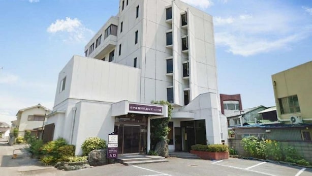 A modern building with a prominent entrance, a parking lot, and a clear sky. - Hotel Niihama Hills Prince House (Niihama)